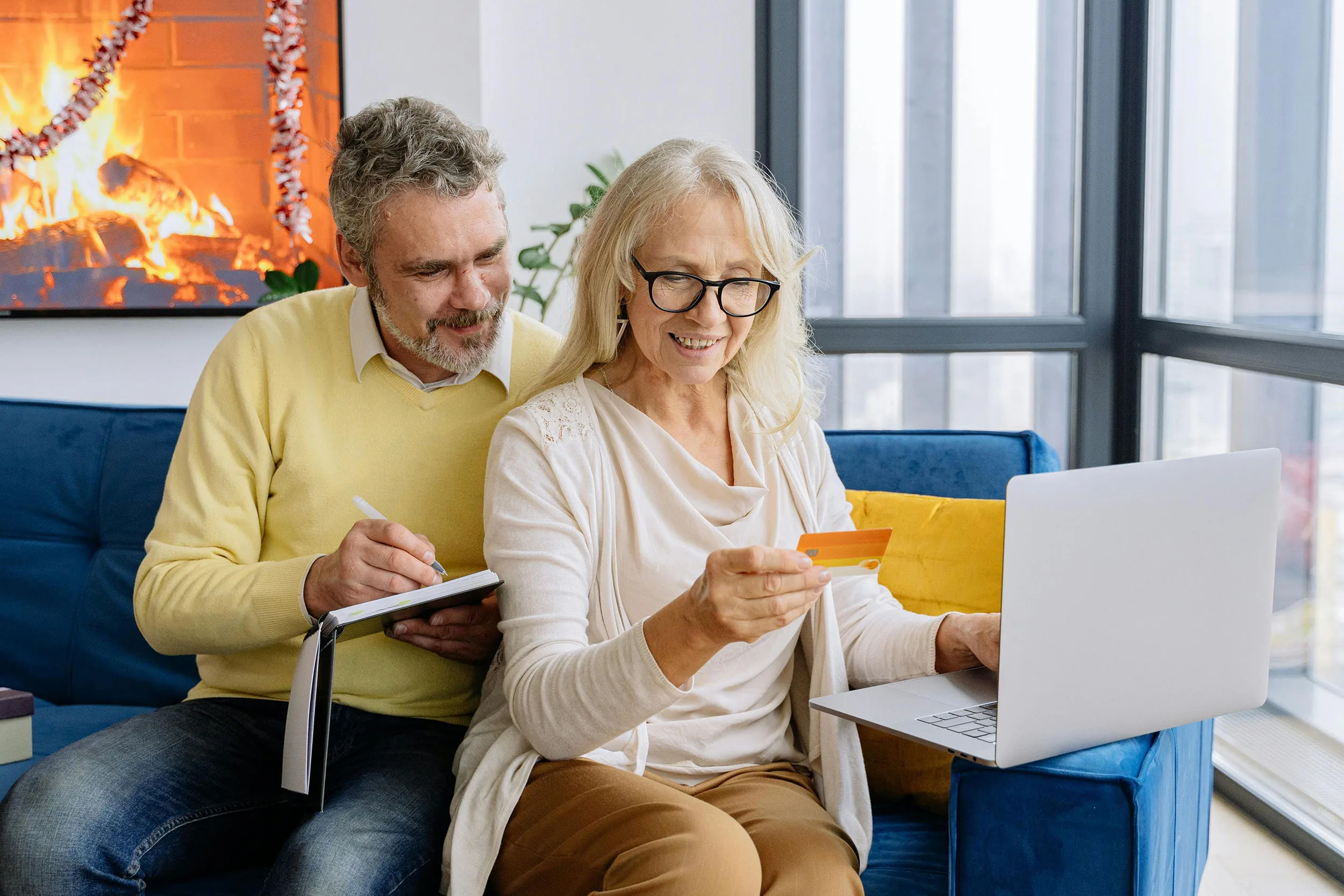 Senior couple managing their budget online by the fireplace.