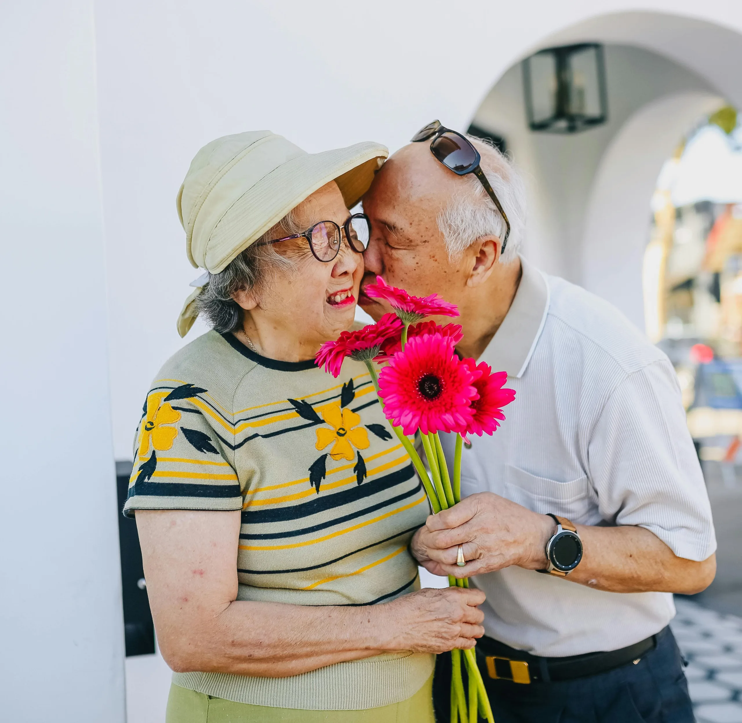 Elderly couple embracing and holding bright pink flowers.